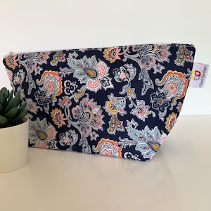 May include: A navy blue zipped pouch featuring a multi-coloured paisley pattern in shades of pink, orange, yellow, and light blue. A white fabric tag on the side displays the text Carol Tye Bags with a small red and yellow logo icon.