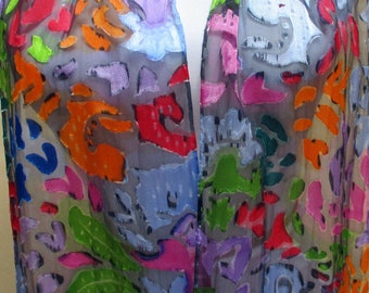 May include: A sheer scarf with a colorful abstract pattern. The pattern features shades of blue, green, orange, pink, and red on a gray background.
