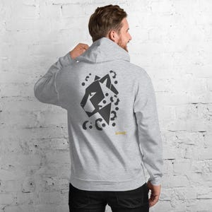May include: A light gray hooded sweatshirt featuring a dark gray geometric panther head graphic on the back. The design includes scattered circular spots and the yellow text No Cosmic printed near the bottom right of the graphic.