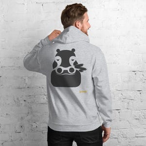 May include: A light gray hooded sweatshirt featuring a dark gray graphic of a stylized hippopotamus head on the back. The hippo design includes white circular eye details and a small yellow text logo reading No Comment positioned below the graphic.