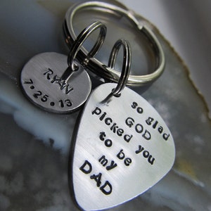 May include: Silver keychain with two charms. One charm is a round disc with the text "Ryan 7.25.13". The other charm is a guitar pick shape with the text "so glad GOD picked you to be my DAD".