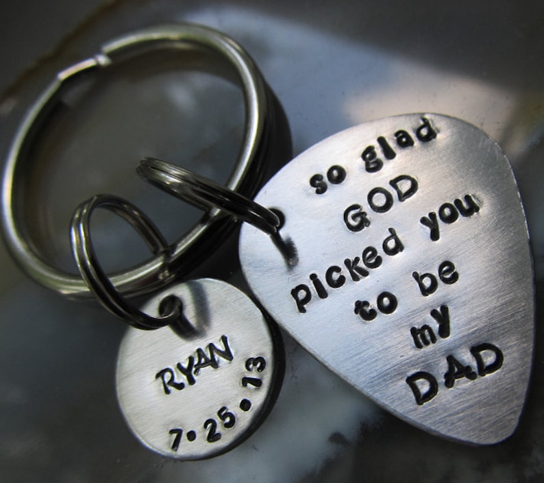 May include: Silver guitar pick keychain with the text "so glad GOD picked you to be my DAD". A smaller silver disc keychain with the text "RYAN 7.25.13" is attached.