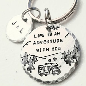 May include: Silver keychain with two tags. One tag is round and says "Life is an adventure with you" with a camper van, trees, and mountains. The other tag is round and says "J & L".