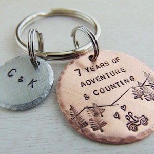 Puede incluir: Un llavero de cobre con el texto "7 Years of Adventure & Counting" y una peque&ntilde;a silueta de jeep. El llavero tambi&eacute;n incluye un dije de plata con las iniciales "C & K".