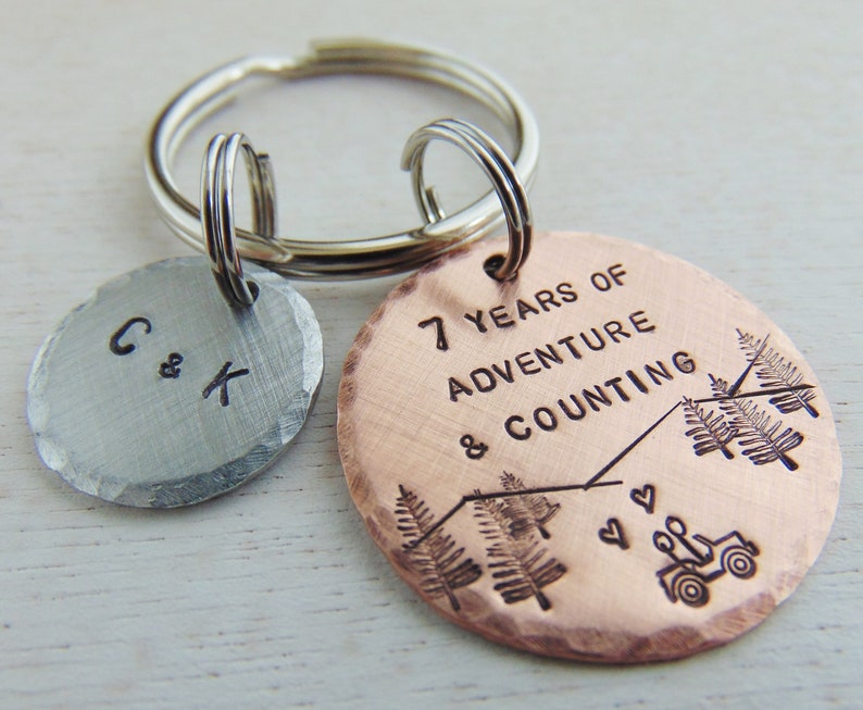 Puede incluir: Un llavero de cobre con el texto "7 Years of Adventure & Counting" y una peque&ntilde;a silueta de jeep. El llavero tambi&eacute;n incluye un dije de plata con las iniciales "C & K".