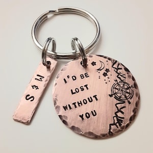 May include: A copper keychain with a round charm that says "I'd be lost without you" and a compass design. The charm is attached to a silver key ring with a smaller rectangular charm that says "S & M".