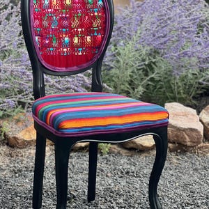 May include: A black wooden chair with curved legs and a rounded backrest. The backrest features a red fabric panel with a multi-colored woven pattern. The seat is upholstered in a vibrant, multi-colored striped fabric with horizontal lines.