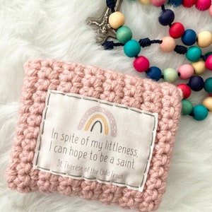 Peut inclure: Une pochette en crochet rose avec un patch en tissu blanc repr&eacute;sentant un arc-en-ciel et la citation "Malgr&eacute; ma petitesse, j'esp&egrave;re &ecirc;tre sainte. Sainte Th&eacute;r&egrave;se de l'Enfant J&eacute;sus."