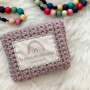 Peut inclure: Une pochette en crochet violet avec un patch en tissu blanc qui dit "Soyez forts et courageux Deut&eacute;ronome 31:6" avec un arc-en-ciel et des &eacute;toiles.