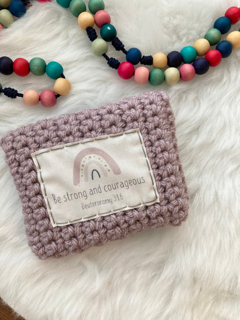 Peut inclure: Une pochette en crochet violet avec un patch en tissu blanc qui dit "Soyez forts et courageux Deut&eacute;ronome 31:6" avec un arc-en-ciel et des &eacute;toiles.