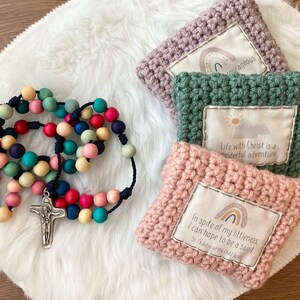 Peut inclure: Un chapelet en bois color&eacute; avec un crucifix en argent, trois pochettes en crochet avec des citations inspirantes et des motifs arc-en-ciel. Les citations sont "Malgr&eacute; ma petitesse, j'esp&egrave;re &ecirc;tre sainte. Sainte Th&eacute;r&egrave;se de l'Enfant J&eacute;sus", "La vie avec le Christ est une merveilleuse aventure", et "Courageux".