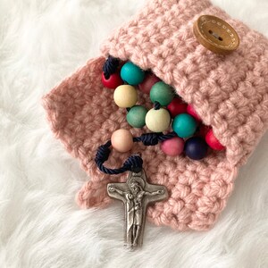 Peut inclure: Une pochette en crochet rose avec un bouton en bois, contenant un chapelet en perles de bois color&eacute;es avec un crucifix en argent.