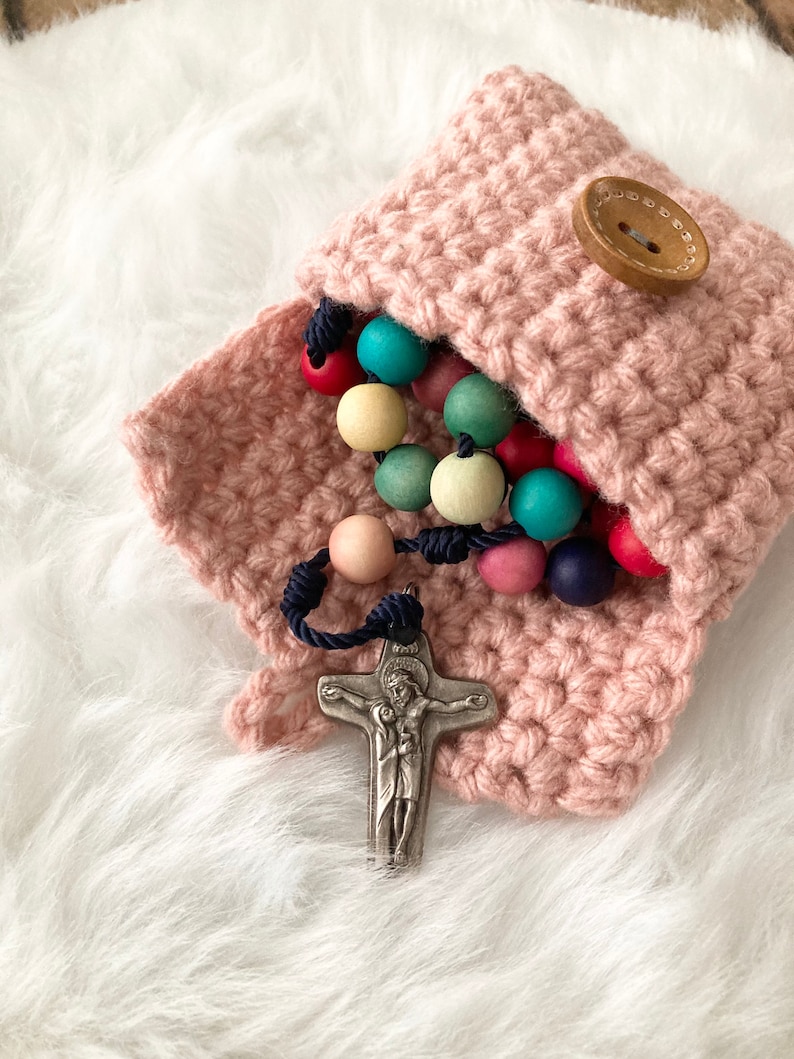 Peut inclure: Une pochette en crochet rose avec un bouton en bois, contenant un chapelet en perles de bois color&eacute;es avec un crucifix en argent.