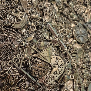 May include: A large collection of assorted silver-toned metal charms in various shapes including a martini glass, a globe, a clock face, and circular pendants with text such as dream, Lord, and our heart filled enough to restart it.