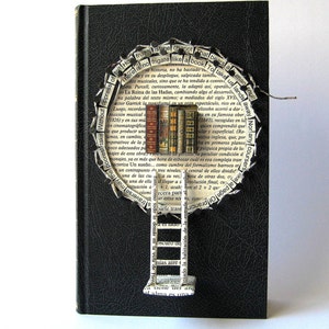 May include: A black book with a circular design made of torn pages. The design features a ladder leading up to a tree with books as leaves. The text on the pages reads "There is no frigate like a book to take us lands away." and "Human soul!"