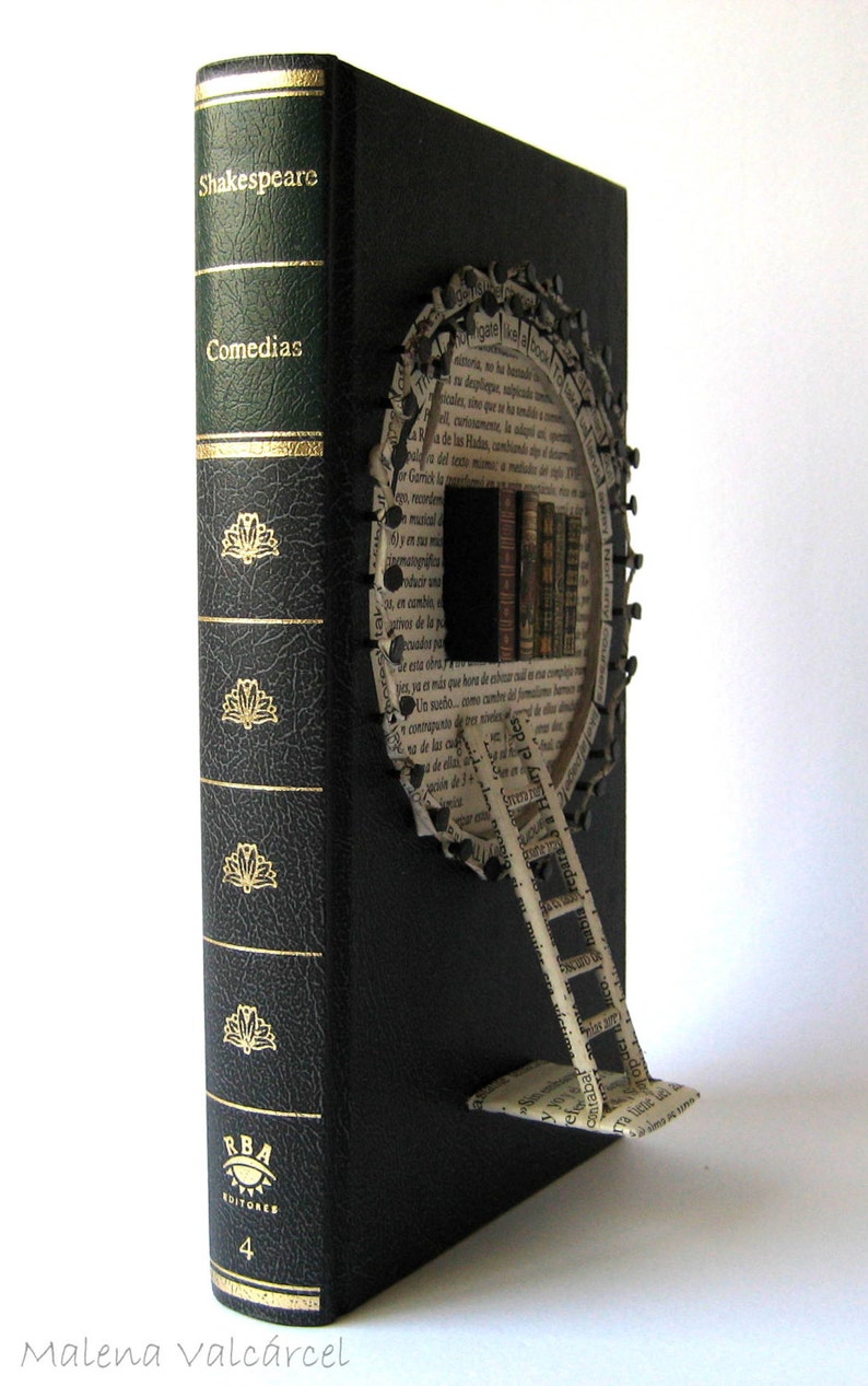 May include: A black book with a gold spine and a paper wheel attached to the front cover. The wheel is made of pages from a book and has a ladder attached to it. The book's spine has the text "Shakespeare Comedias" and "RBA Editores 4".