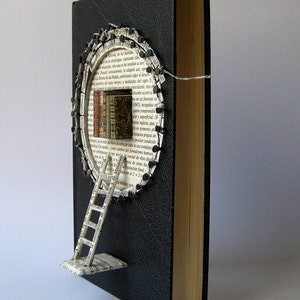 May include: A black book with a circular opening in the cover. The opening is filled with pages from a book, forming a ladder leading up to a small stack of books. The text "Malena valc&aacute;rcel" is printed at the bottom of the image.