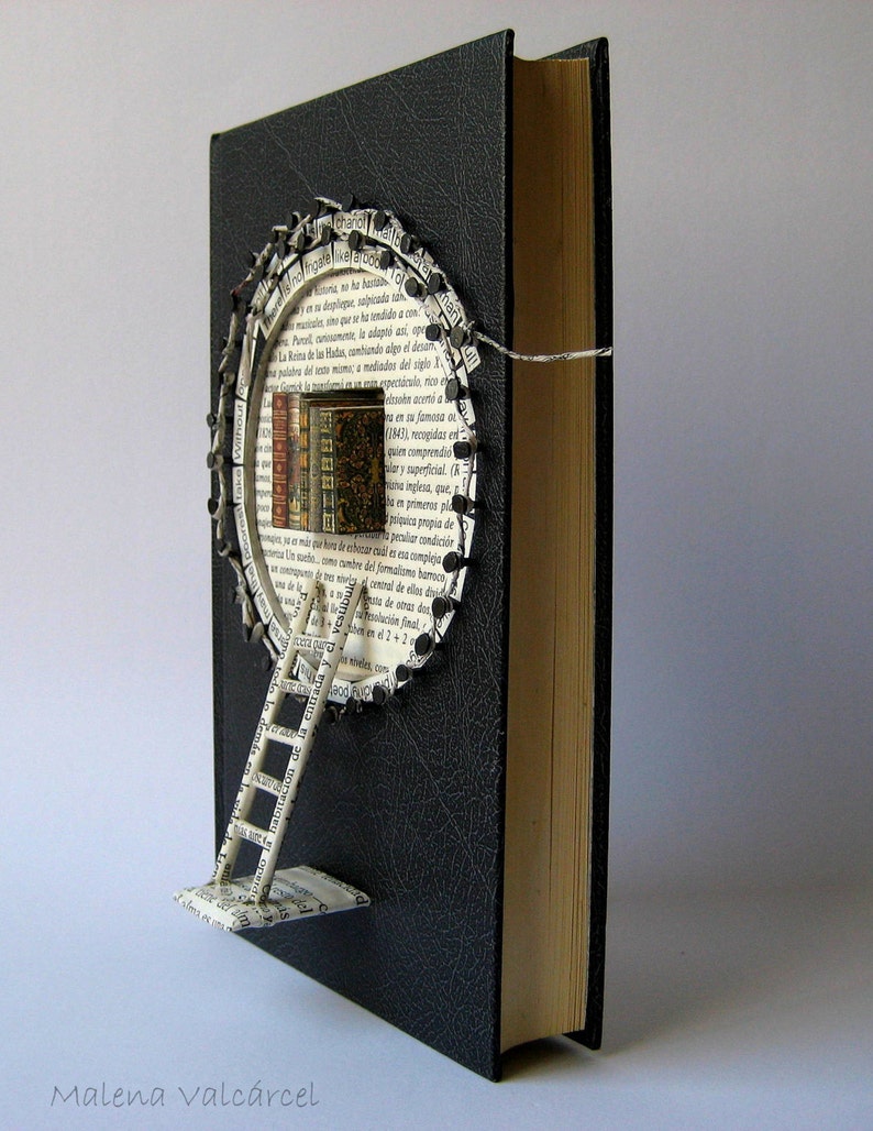 May include: A black book with a circular opening in the cover. The opening is filled with pages from a book, forming a ladder leading up to a small stack of books. The text "Malena valc&aacute;rcel" is printed at the bottom of the image.