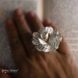 Peut inclure: Une fleur en papier fabriqu&eacute;e &agrave; partir des pages d'un livre. La fleur est blanche et pr&eacute;sente un design d&eacute;licat et superpos&eacute;. La fleur est tenue par la main d'une personne.
