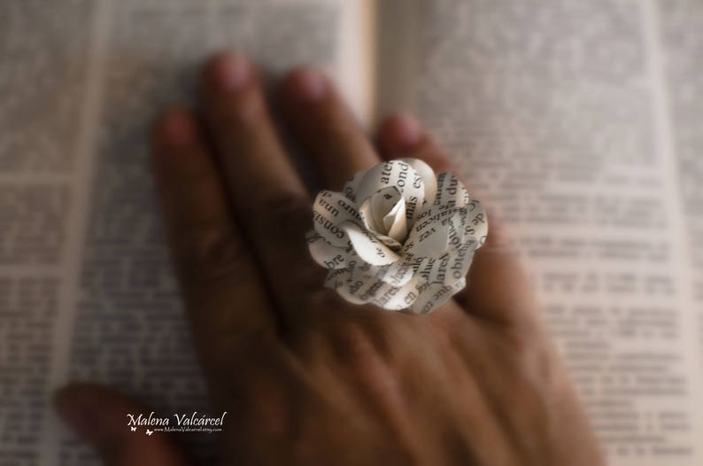 Peut inclure: Une fleur en papier fabriqu&eacute;e &agrave; partir des pages d'un livre. La fleur est blanche et pr&eacute;sente un design d&eacute;licat et superpos&eacute;. La fleur est tenue par la main d'une personne.