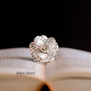 Peut inclure: Une fleur en papier blanche, r&eacute;alis&eacute;e &agrave; partir des pages d'un livre, avec du texte noir, est plac&eacute;e sur un livre ouvert. Le livre est ferm&eacute; et la fleur est au centre des pages ouvertes.