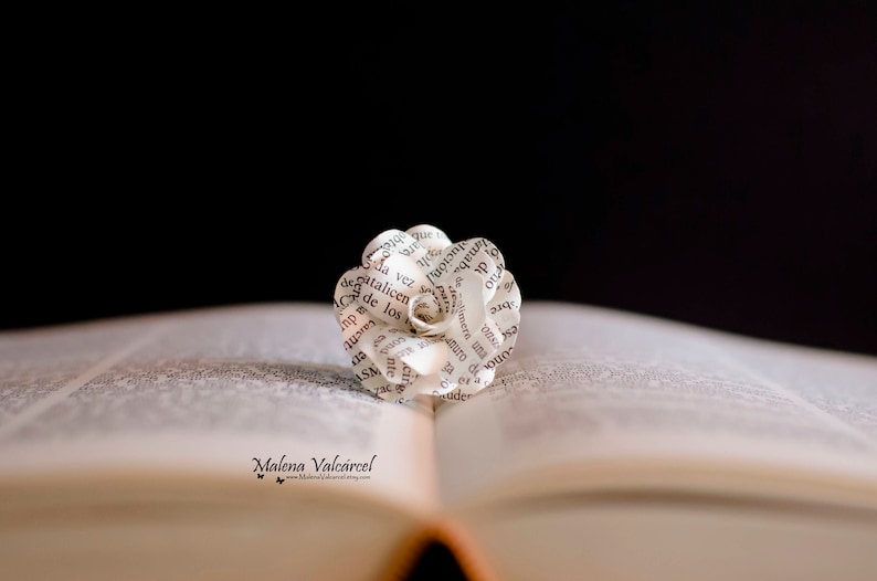 Peut inclure: Une fleur en papier blanche, r&eacute;alis&eacute;e &agrave; partir des pages d'un livre, avec du texte noir, est plac&eacute;e sur un livre ouvert. Le livre est ferm&eacute; et la fleur est au centre des pages ouvertes.