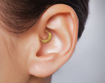 May include: A gold-colored beaded hoop earring in a person's ear. The hoop is worn in the upper cartilage of the ear.