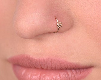May include: A close-up of a person's nose with a small gold nose ring featuring a flower design.
