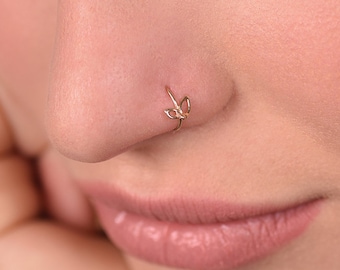 May include: A close-up of a person's nose with a gold nose ring featuring a delicate leaf design.