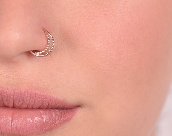 May include: Close-up of a person's face with a small, gold, double hoop nose ring. The person has brown eyes and dark hair.