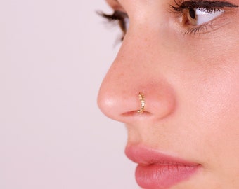 May include: A close-up of a person's face with a gold nose ring. The ring is a simple band with a small, decorative design.