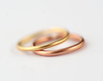 May include: Two simple wedding bands, one gold and one rose gold, are stacked on top of each other.