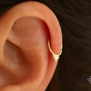 May include: A gold hoop earring with a small triangle charm. The triangle has a textured surface and is set with tiny diamonds.
