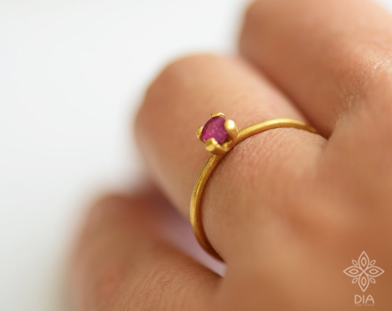 May include: A delicate gold ring with a small, round, pink gemstone set in a simple, claw setting.
