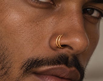 May include: A double hoop nose ring crafted from polished gold-toned metal. The jewelry features two thin, circular bands that sit side-by-side, creating a layered appearance when worn in the nostril. The design is simple, smooth, and metallic.