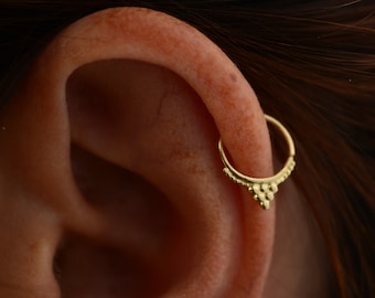 May include: Gold hoop earring with a textured, triangular design. The earring is worn in the upper cartilage of the ear.