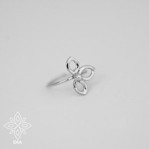 May include: A silver ring shaped like a flower with a small bead in the centre.