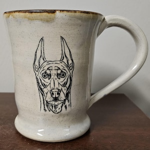 May include: White ceramic mug with a black and white illustration of a Doberman Pinscher's face.