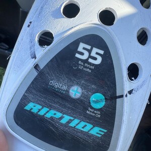 May include: A white plastic motor housing featuring a black and gray control panel with the text 55 lbs. thrust 12 volts, digital maximizer, and RIPTIDE. The panel includes a plus symbol, a circular teal indicator, and the text Test with Motor Off.