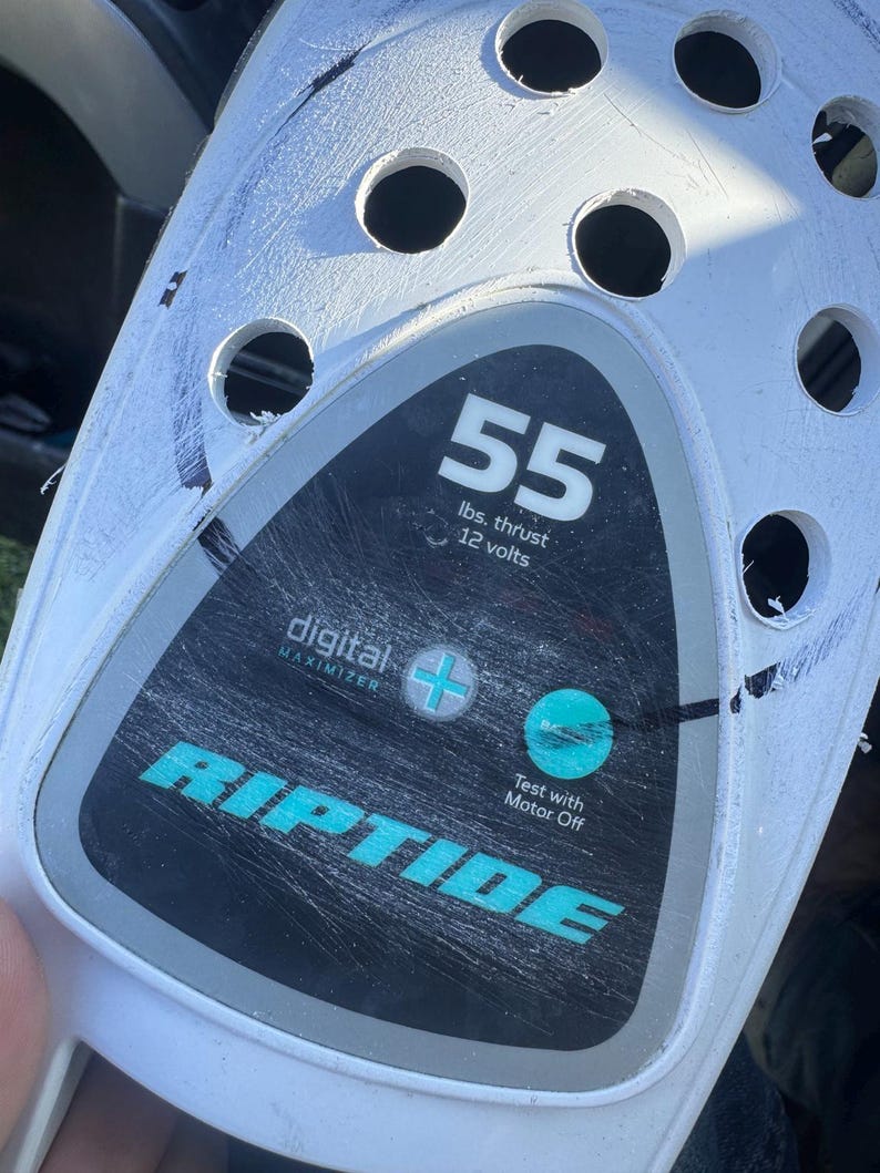 May include: A white plastic motor housing featuring a black and gray control panel with the text 55 lbs. thrust 12 volts, digital maximizer, and RIPTIDE. The panel includes a plus symbol, a circular teal indicator, and the text Test with Motor Off.