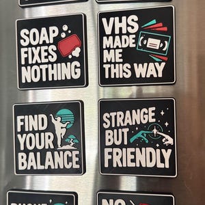 May include: Eight square black magnets with white text and colorful graphic icons. The text includes phrases like Raised on Cult Classics, Reality Needs a Reboot, Soap Fixes Nothing, VHS Made Me This Way, Find Your Balance, Strange But Friendly, Phone Home Later, and No Mercy for Mondays.