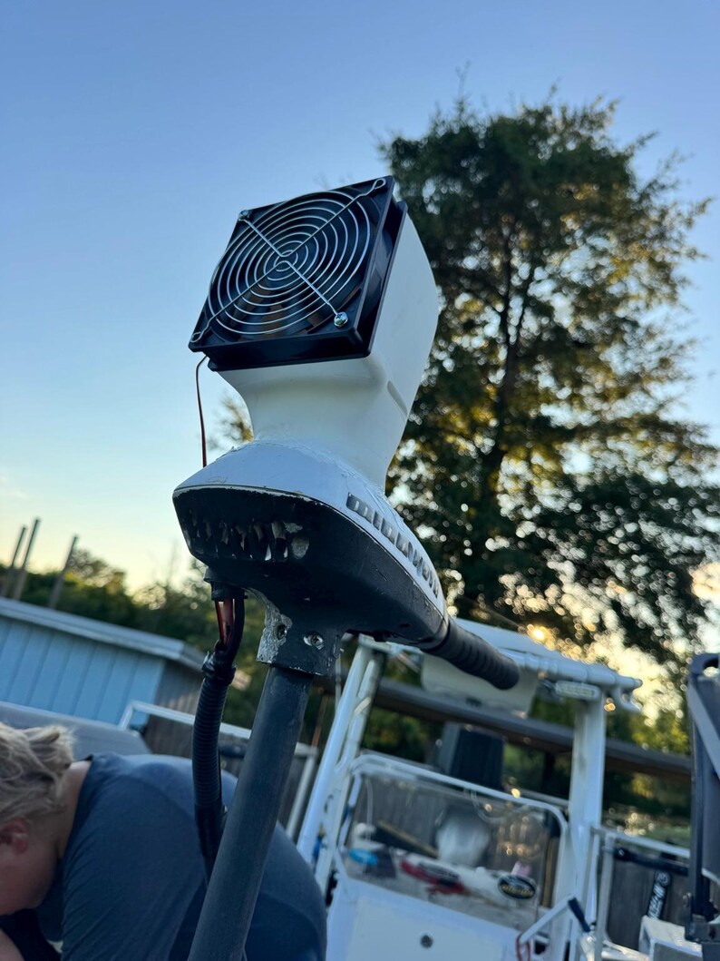 May include: A white trolling motor head unit featuring a black cooling fan mounted on top with a circular metal wire grill. The motor housing displays the brand name Minn Kota in black lettering on the side, connected to a vertical shaft.