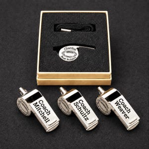 A set of three personalized whistle blowers, each with a name engraved on it, placed on a black surface.