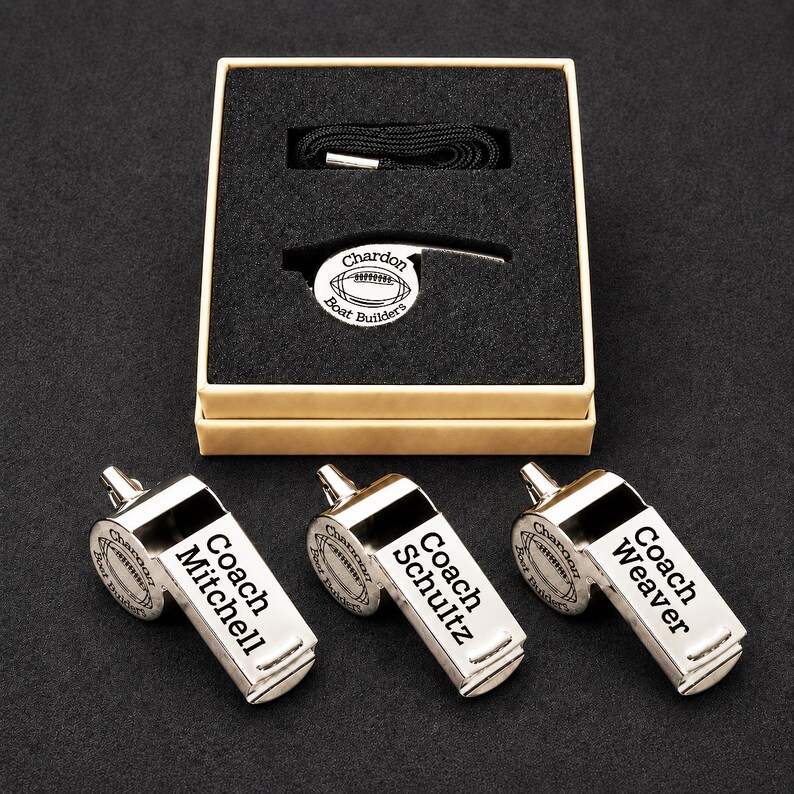 A set of three personalized whistle blowers, each with a name engraved on it, placed on a black surface.