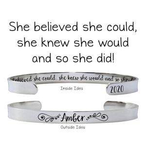 May include: A silver-colored cuff bracelet with the text "She believed she could, she knew she would and so she did!" above it. The inside of the bracelet reads "believed she could, she knew she would and so she did" and "2020". The outside reads "Amber."