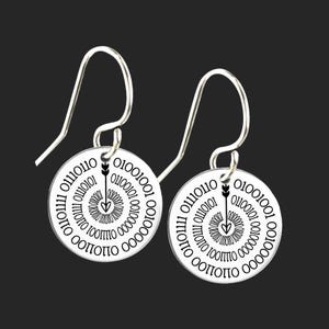Puede incluir: Un par de pendientes de plata con un diseño circular que presenta una espiral de código binario y una flecha que apunta a un corazón. Los pendientes tienen un cierre de gancho.