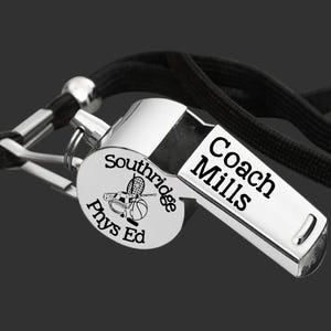 Può includere: Fischietto d'argento con un laccio nero. Il fischietto ha un design inciso con il testo "Coach Mills" e "Southridge Phys Ed" insieme a una grafica di un'ape con attrezzature sportive.