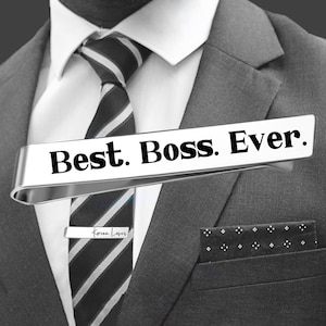 May include: Silver tie bar with the text "Best. Boss. Ever." in black lettering. The tie bar is worn on a white shirt with a black and white striped tie.