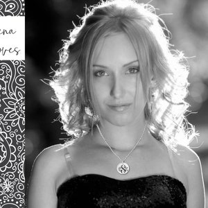 May include: A black and white portrait of a woman with long, wavy hair. She is wearing a black dress and a silver necklace with a monogram pendant.