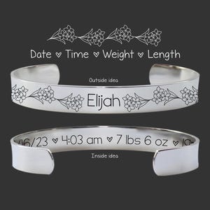 May include: Silver bangle bracelet with an engraved floral design and the name Elijah. The inside of the bracelet is engraved with the date 06/23, time 4:03 am, weight 7 lbs 6 oz, and length 19 inches.